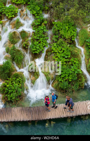 Wanderer ein Spaziergang entlang der Holzsteg, Kaskaden von Wasser, ausgegossen in die azurblauen See Kaluđerovac an den Plitvicer Seen Nationa Stockfoto