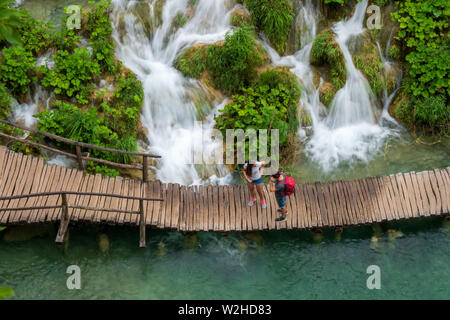 Wanderer ein Spaziergang entlang der Holzsteg, Kaskaden von Wasser, ausgegossen in die azurblauen See Kaluđerovac an den Plitvicer Seen Nationa Stockfoto