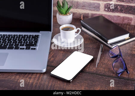 Laptop Notebook mit leerer Bildschirm und Tasse Kaffee und Notizblock Stift und Bücher und Smart-phone auf hölzernen Tisch. Mock up auf Holztisch mit Laptop wi Stockfoto