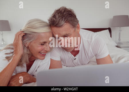 Active Senior Paar mit Laptop im Bett im Schlafzimmer an komfortables Zuhause liegen Stockfoto