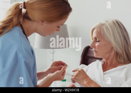 Ärztin sprechen auf disabled Active Senior Frau über ihre Hörgeräte auf dem Bett im Schlafzimmer Stockfoto