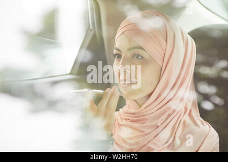 Lächelnd selbstbewussten jungen muslimischen Geschäftsfrau im schönen hijab Aufnahme audio Nachricht beim Reiten Auto, hinter Glas anzeigen Stockfoto