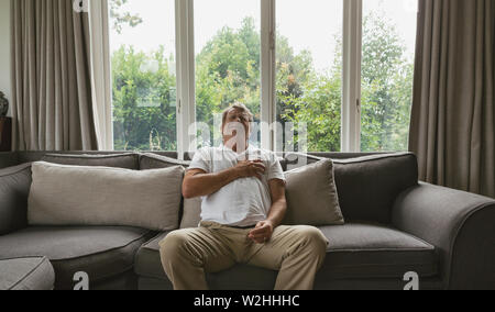 Aktive ältere Menschen leiden unter Schmerzen in der Brust auf dem Sofa in ein gemütliches Heim Stockfoto