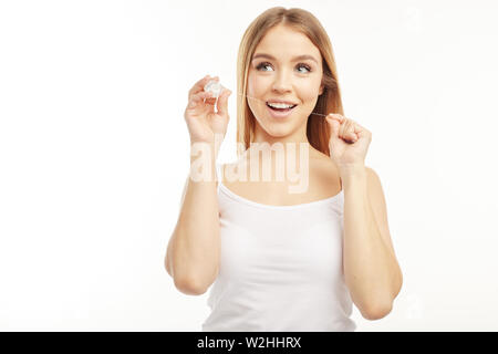 Lächelnde Blondine auf dem weißen Hintergrund zeigen, wie Zahnseide zu verwenden, die Sie in Ihrer Hand hält. Stockfoto