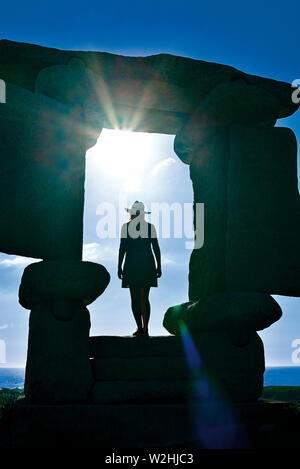 Silhouette einer Frau, die in einer natürlichen Stein gerahmte Fenster auf das Meer und auf die Sonne Stockfoto