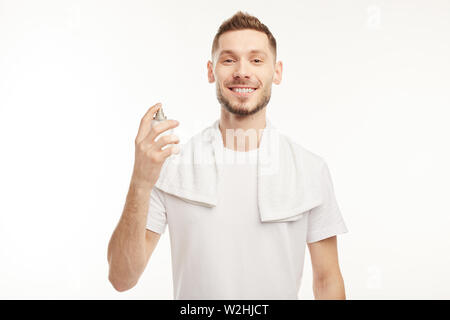 Junge bärtige Mann auf dem weißen Hintergrund sprays Parfüm auf sich. Stockfoto