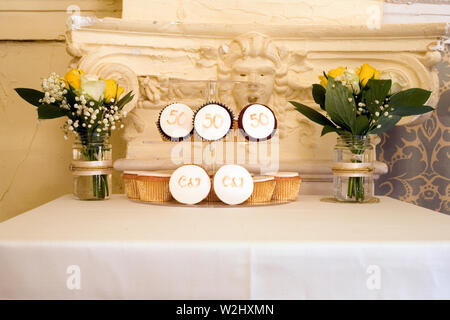 Anzeige der Tabelle mit Gläsern von Blumen und Mini iced Kuchen zum 50. Hochzeitstag feiern ein Paar Stockfoto