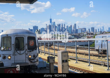 F Zug in die Smith-9th Street erhöhten U-Bahnstation mitdem Lower Manhattan Skyline am Horizont in der gowanus Nachbarschaft von Brooklyn, New York. Stockfoto