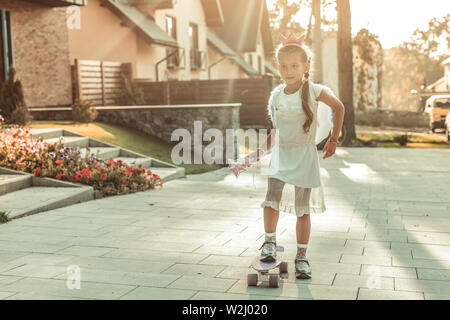 Resolute junge Dame im weißen Kleid reiten auf einem Skateboard Stockfoto