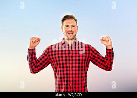 Jubelnde Menschen zujubeln, ein persönlicher Erfolg lachen und Pumpen die Luft mit beiden Fäusten in einer oberen Körper frontale Ansicht über das Sky Stockfoto