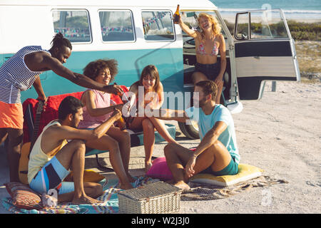 Gruppe von Freunden toasten Bierflasche in der Nähe von Camper am Strand Stockfoto