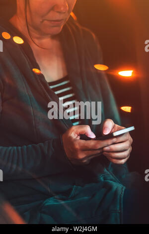 Frau SMS auf Handy im Auto in der Nacht auf einem Parkplatz, Erwachsene weibliche Person mit Smartphone für Kommunikation, selektiven Fokus Stockfoto