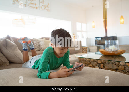 Junge spielt Spiel auf Mobiltelefon von Sofa zu Hause liegen Stockfoto