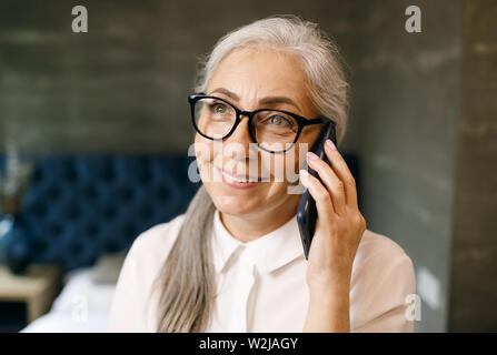 Lächelnde ältere Frau mit weißen Haaren in Brillen sprechen auf dem Smartphone Stockfoto