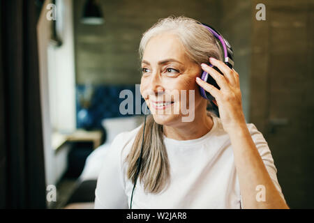 Grauen Haaren ältere Frau trägt Kopfhörer Anhören der Musik, im Innenbereich home Schuß Stockfoto