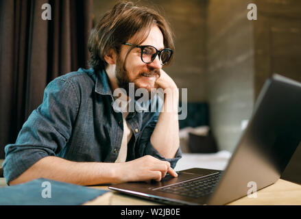 Junge lächelnde bärtiger Mann Brille etwas aufpassen am Notebook Stockfoto