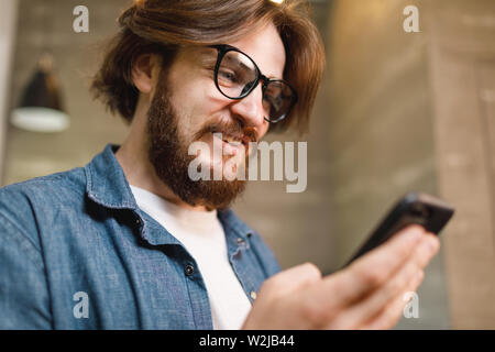 Bärtiger Mann mit Brille lächelnd, während sie Smartphone Stockfoto