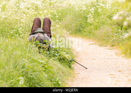 Person mit einem Hut im Gesicht und einem Trekking Stock auf einer Seite ruhen auf einer Bank in einem Land Park im Sommer Stockfoto