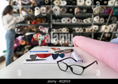 Mädchen wählt ein Material von Regalen mit bunten Stoff Rollen in einer Lagerhalle. Vor ihr es gibt weißen Tisch mit Textil- Stücke und ein Stockfoto