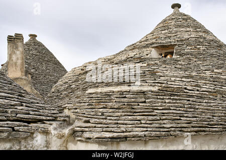 Konischen Dächern der Trulli auf dem Himmel Hintergrund in Alberobello Stadt in Italien. Es gibt Kamine und eine bunte Katze in der Nähe der Fenster openi Stockfoto