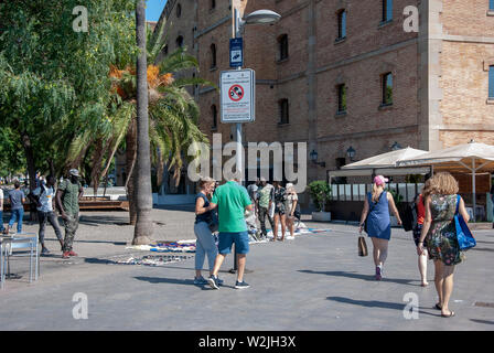 Migrant Straße Händler krass, Güter zum Verkauf Moll de Diposit Port Vell Marina Barcelona Spanien unter Warnschild Beratung nicht kaufen Stockfoto