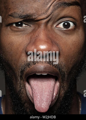 Nahaufnahme, Porträt der jungen und emotionale african-american man. Sehr detail photoshot der männlichen Modell mit gepflegter Haut und Gesichtsausdruck. Konzept der menschlichen Emotionen. Mit der Zunge heraus hängen. Stockfoto