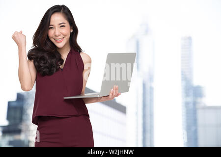 Portrait einer aufgeregt asiatische Frau mit Laptop und feiert Erfolg über Gebäude Hintergrund, Anheben der Arme mit einem Blick der Glück, Fe Stockfoto