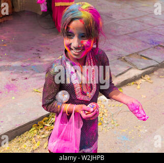 Eine glückliche kleine indische Mädchen an der Hindu Holi Festival in Jaipur Indien bedeckt mit den bunten Pulver (Gula) mit einer Tasche von Pink Power auf ihrem Arm Cele Stockfoto
