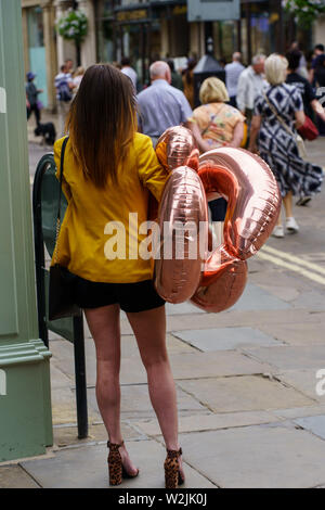 Frau stand an der Straßenecke mit zwei neuen Geburtstagsballons, York, North Yorkshire, England, Großbritannien. Stockfoto