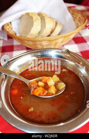 Eine Schüssel mit Traditionelle Ungarische Gulaschsuppe mit einem Korb mit Brot. Gulasch ist das Nationalgericht der Ungarn. Stockfoto