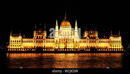 Das ungarische Parlament Gebäude neben der Donau, ist abends beleuchtet. Stockfoto