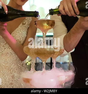 Nahaufnahme einer Kaskade Champagner Brunnen von Bräutigam und Braut am Bankett Hintergrund. Neu verheirateten gießen Sekt in die Gläser Turm Stockfoto