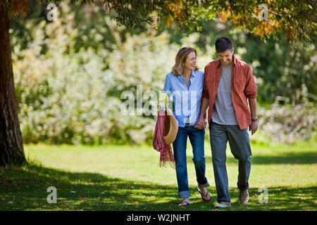 Glückliches Paar mittleren Alters gehen Hand in Hand durch einen grünen Park. Stockfoto