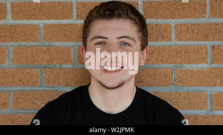 Eine junge ziemlich blass dunkelhäutige Mann mit einem schwarzen T-Shirt, kurze lockige Rotbraune Haare, blaue Augen, eine große Seele Patch und ein großes strahlendes Grinsen. Stockfoto