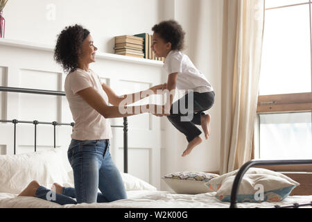 Gerne afrikanische Mama spielen mit Kind Junge sprang auf dem Bett Stockfoto