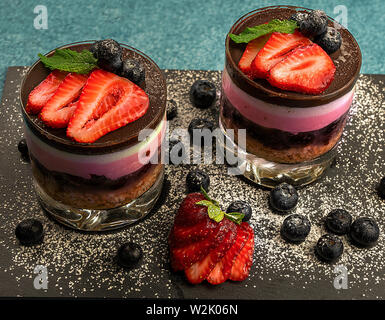 Mousse von Biskuit, Kirschen, Ananas und überdachte Schokolade mit Sahne von Schokolade, Blaubeeren und Erdbeeren. Stockfoto