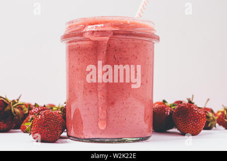 Dicke texturierte Erdbeere Smoothie in Glas Glas mit Stroh und reife Beeren auf weißem Hintergrund, close-up. Stockfoto