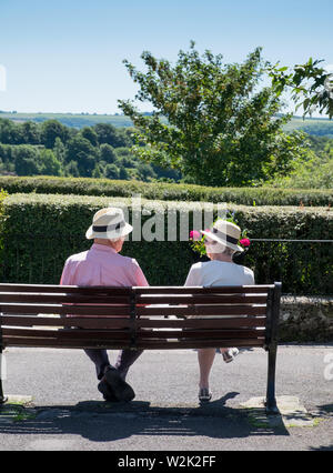 Ältere Rentnerehepaar entspannen auf einer Parkbank, die an der Ansicht von Blackmore Vale in Shaftesbury, Dorset Stockfoto