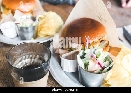 Handwerk Rindfleisch Burger mit Gemüse auf einem Teller mit Pommes und Salat auf einem Holztisch. Stockfoto