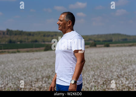 Portrait von Stattlichen älterer Mann im Außenbereich. Sportliche athletische älterer Mann auf dem Hintergrund von Himmel und Baumwolle. Senior Bauer stehen in der Wiese Hintergrund. Stockfoto