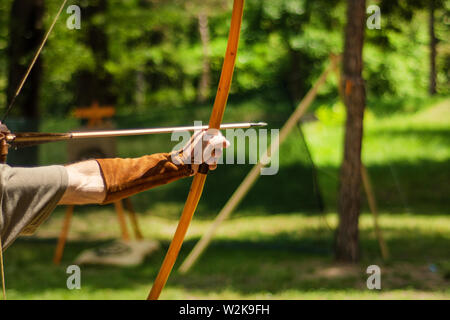 Man mittelalterliche Archer Hand hält seinen Bogen mit Pfeil und mit dem Ziel der Ziel Aktivität im Freien im Wald. Mittelalterliche Sport Konzept. Nahaufnahme Stockfoto