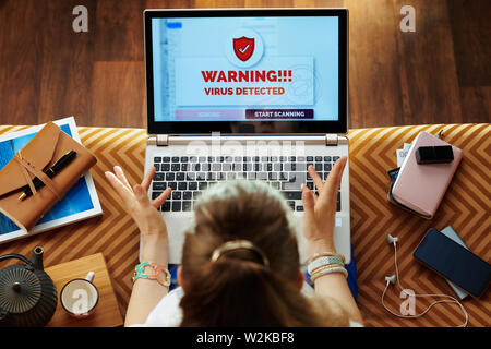 Obere Ansicht genervt elegante Frau sitzt auf einem Sofa in der modernen Wohnzimmer mit Virus auf einem Laptop. Stockfoto