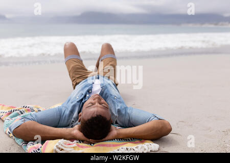 Mann schlafen mit den Händen hinter dem Kopf am Strand Stockfoto