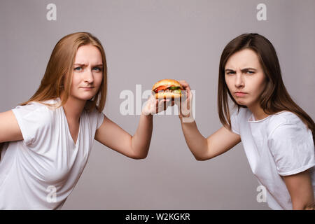 Zwei runzelte die junge schöne Frau mit Appetitlichen schädlichen Burger an Kamera suchen Stockfoto