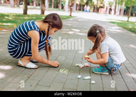 Zwei süße kleine Mädchen sitzen und Zeichnen mit Kreide auf Asphalt im Park im Sommer Tag Stockfoto