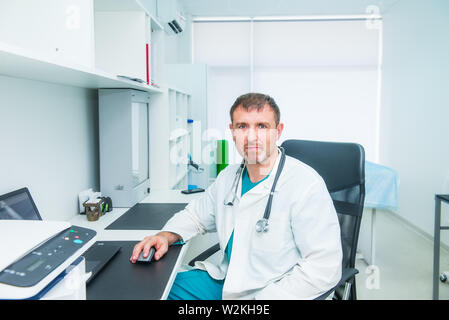 Portrait der männlichen reife Arzt Gefühl in sich zuversichtlich sitzend auf seinem Arbeitsplatz und suchen an der Kamera. Medizin und Gesundheit Konzept. Occ Stockfoto