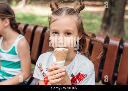 Hübsches kleines Mädchen sitzt auf der Bank und essen ein Eis im Freien Stockfoto