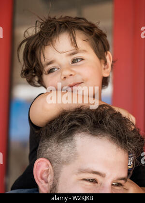 Ein Kind sitzt auf den Schultern eines Erwachsenen auf South Street in South Philadelphia Stockfoto