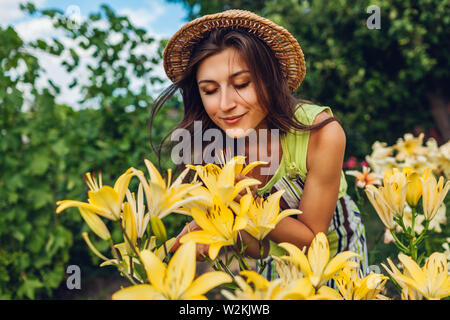 Junge Frau duftende Blumen im Garten. Gärtner kümmert sich um Lilien. Gartenarbeit Konzept Stockfoto