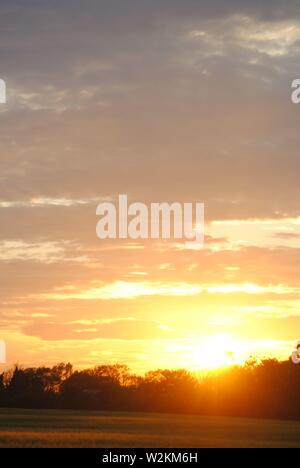Sonnenuntergang über die Felder von Suffolk, Sommer orange-gelbe Sonne mit dunklen Wolken Stockfoto